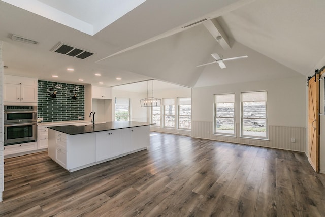 kitchen with a barn door, a kitchen island with sink, white cabinets, and double oven