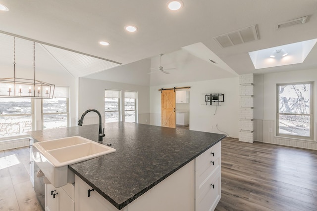 kitchen featuring lofted ceiling, sink, white cabinets, a barn door, and a center island with sink