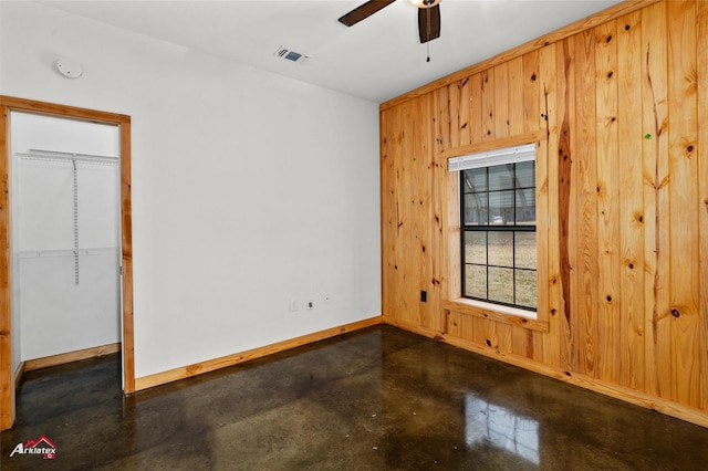 empty room featuring ceiling fan and wooden walls