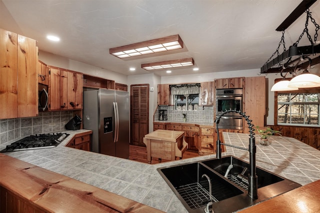 kitchen with pendant lighting, tile countertops, backsplash, kitchen peninsula, and stainless steel appliances