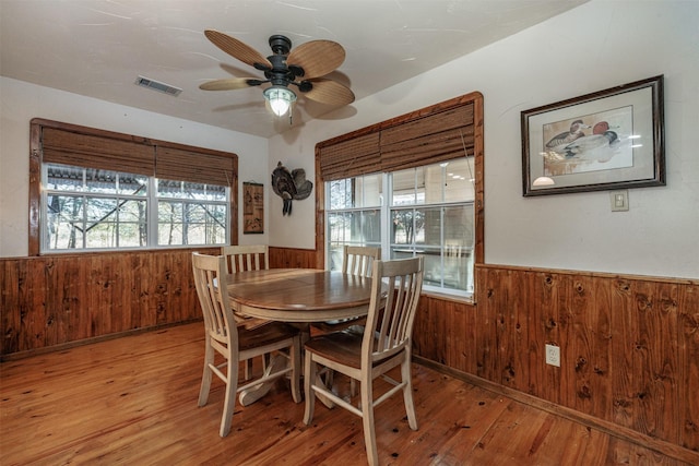 dining area with ceiling fan, light wood-type flooring, and wood walls