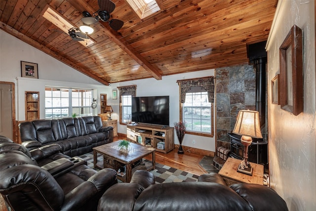 living room with vaulted ceiling with skylight, a wood stove, hardwood / wood-style flooring, ceiling fan, and wood ceiling