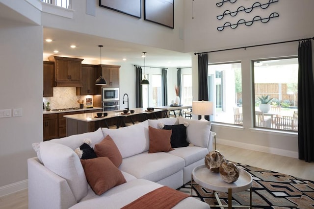 living room with a high ceiling, sink, and light hardwood / wood-style floors