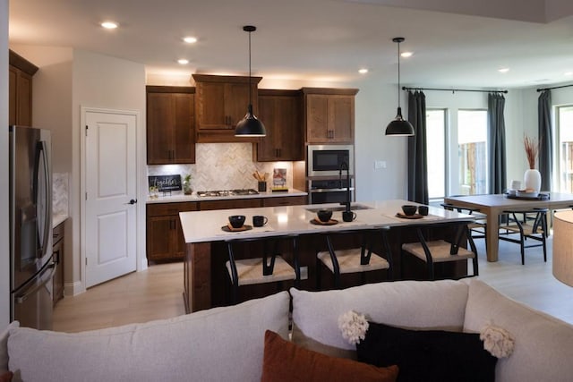 kitchen with sink, decorative light fixtures, stainless steel appliances, and an island with sink