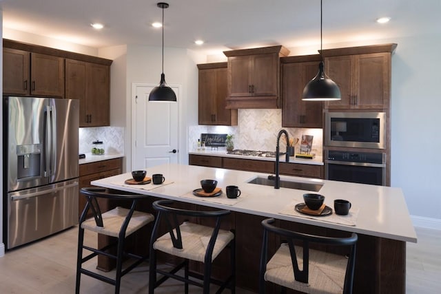 kitchen with sink, light wood-type flooring, stainless steel appliances, and a center island with sink