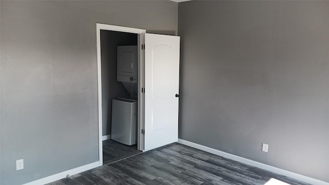 unfurnished bedroom featuring stacked washer and dryer and dark wood-type flooring