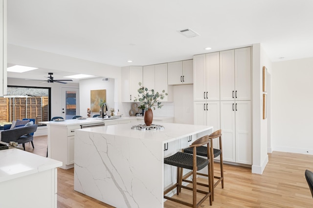 kitchen with a peninsula, a kitchen island, light stone countertops, and light wood-style floors
