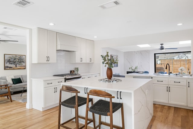 kitchen with sink, light stone counters, a kitchen island, custom range hood, and white cabinets