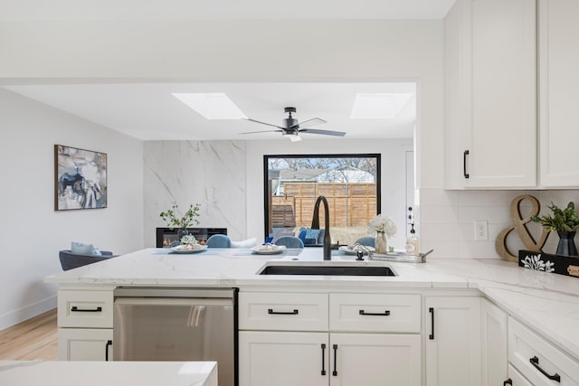 kitchen with tasteful backsplash, white cabinetry, dishwasher, sink, and kitchen peninsula