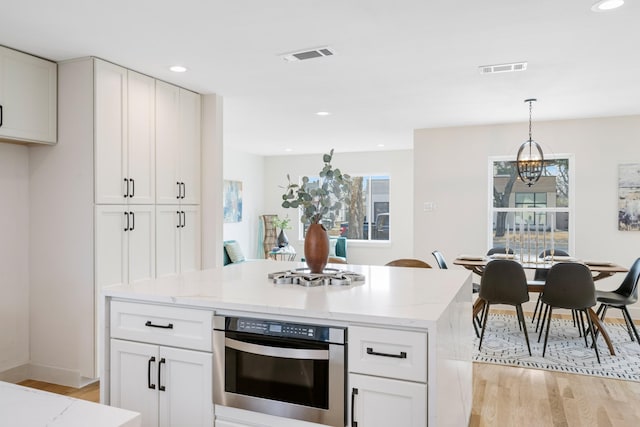 kitchen featuring pendant lighting, white cabinets, light stone counters, and stainless steel oven