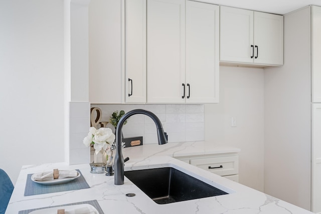 kitchen with light stone counters, backsplash, sink, and white cabinets