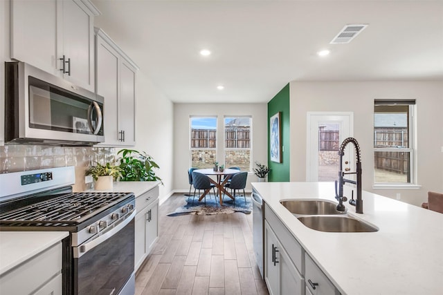 kitchen with sink, hardwood / wood-style flooring, appliances with stainless steel finishes, backsplash, and white cabinets