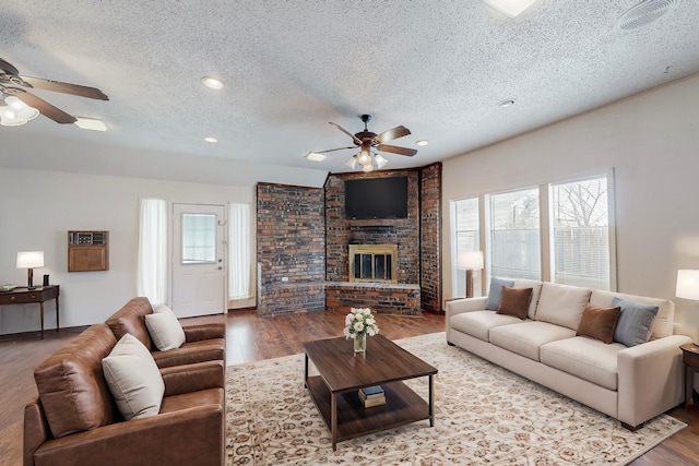 living room with hardwood / wood-style flooring, ceiling fan, a brick fireplace, and a textured ceiling