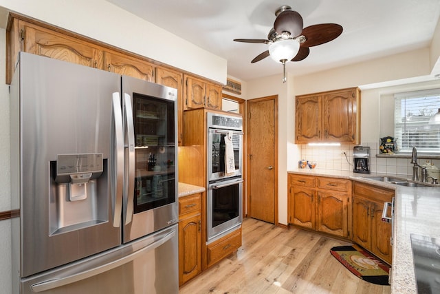 kitchen featuring sink, light hardwood / wood-style flooring, ceiling fan, appliances with stainless steel finishes, and decorative backsplash