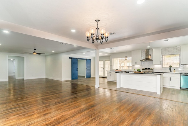 kitchen featuring white cabinets, a barn door, hanging light fixtures, and wall chimney range hood