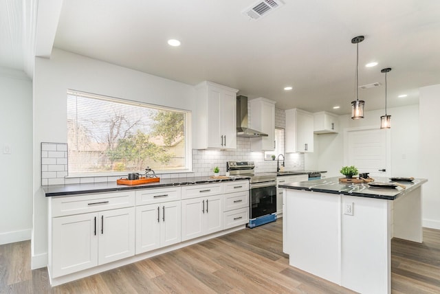 kitchen with electric stove, decorative light fixtures, white cabinetry, a center island, and wall chimney exhaust hood