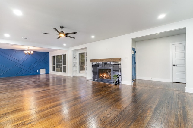 unfurnished living room featuring built in shelves, dark wood-type flooring, and ceiling fan with notable chandelier