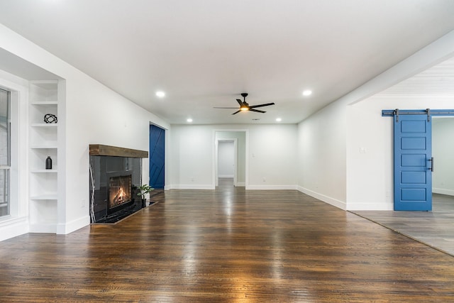 unfurnished living room featuring dark hardwood / wood-style floors, ceiling fan, a barn door, and built in features