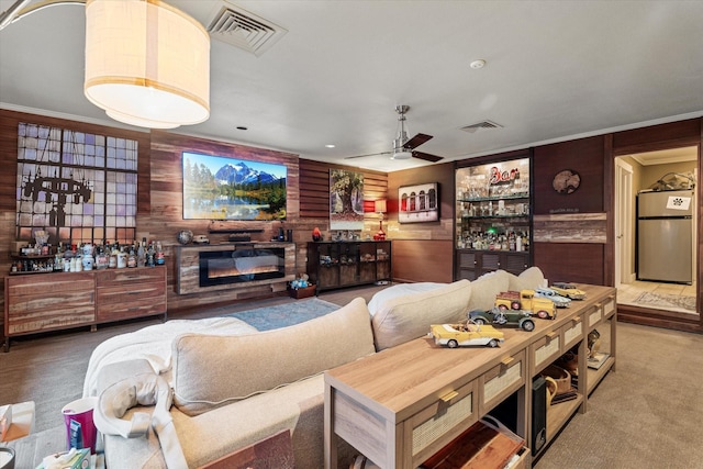 living room with ornamental molding, wood walls, ceiling fan, and carpet