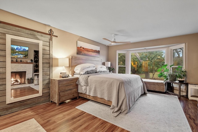 bedroom with wood-type flooring, a fireplace, and ceiling fan