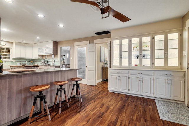 kitchen with dark hardwood / wood-style floors, white cabinetry, a breakfast bar area, decorative backsplash, and ceiling fan