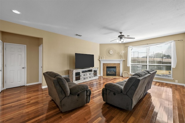 living room with a tile fireplace, dark hardwood / wood-style floors, and ceiling fan