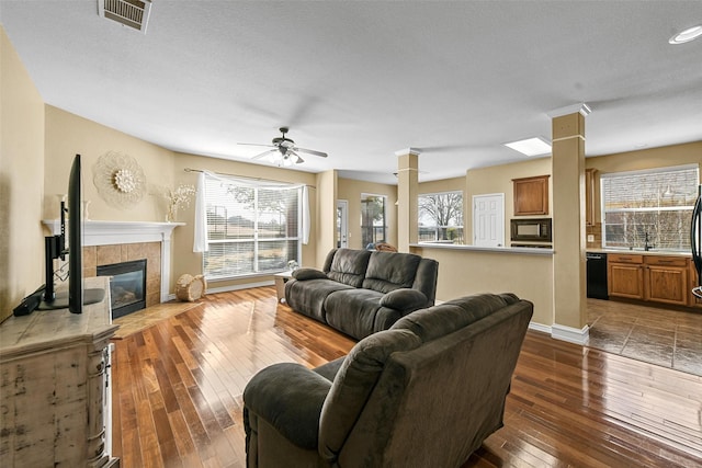 living room with dark hardwood / wood-style flooring, a tiled fireplace, plenty of natural light, and ornate columns