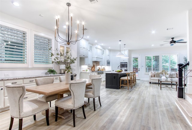 dining space featuring ceiling fan with notable chandelier and light hardwood / wood-style flooring