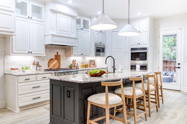 kitchen with white cabinetry, appliances with stainless steel finishes, an island with sink, pendant lighting, and light stone countertops