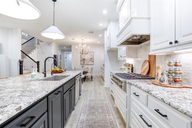 kitchen with sink, an inviting chandelier, hanging light fixtures, white cabinets, and light wood-type flooring