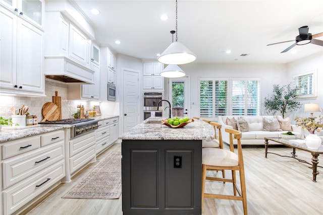 kitchen with white cabinetry, appliances with stainless steel finishes, decorative light fixtures, and a kitchen island with sink