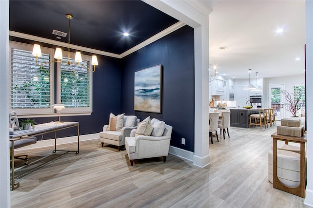 living area with crown molding, an inviting chandelier, and light wood-type flooring