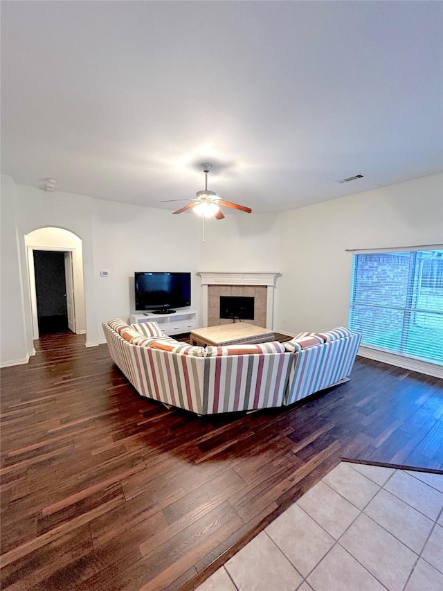 unfurnished living room with ceiling fan, wood-type flooring, and a tiled fireplace