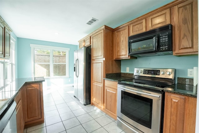 kitchen with light tile patterned floors, stainless steel appliances, and dark stone counters