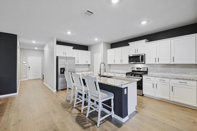 kitchen featuring sink, stainless steel appliances, light stone counters, an island with sink, and white cabinets