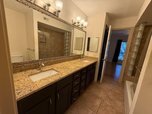 bathroom with vanity, toilet, a textured ceiling, and tiled shower