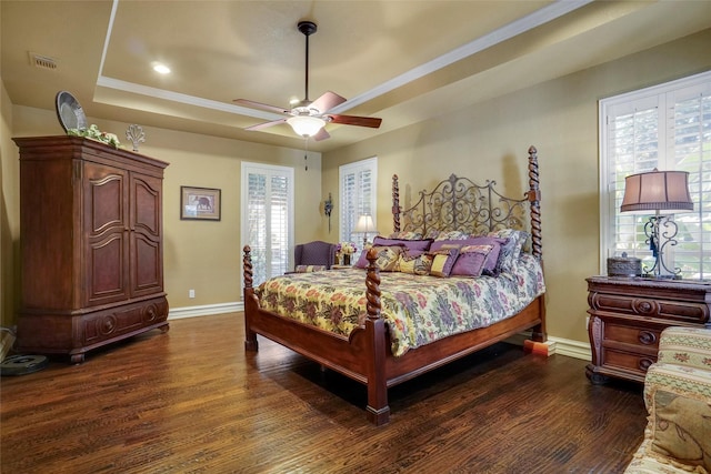 bedroom with dark hardwood / wood-style floors, ceiling fan, and a tray ceiling