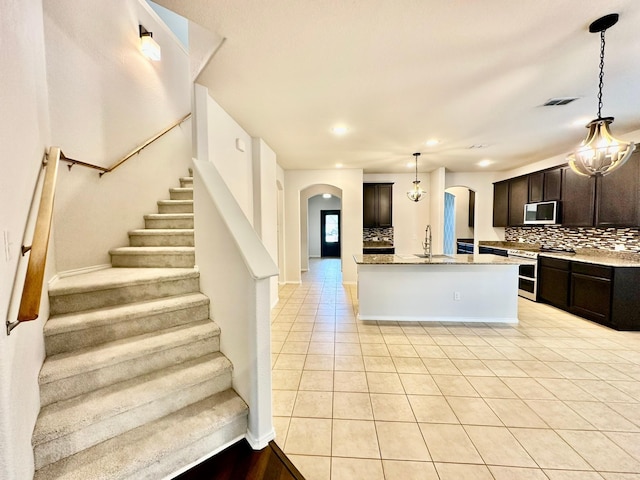 kitchen featuring pendant lighting, sink, backsplash, an island with sink, and range with two ovens