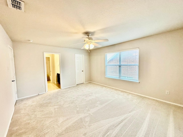 unfurnished bedroom featuring ceiling fan, ensuite bath, light colored carpet, and a textured ceiling