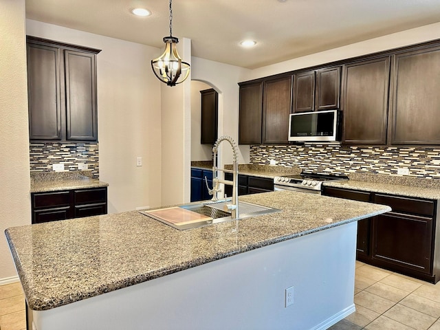 kitchen with appliances with stainless steel finishes, light stone countertops, a kitchen island with sink, and dark brown cabinets