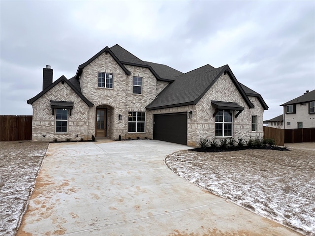 french country style house featuring an attached garage, brick siding, fence, concrete driveway, and a chimney