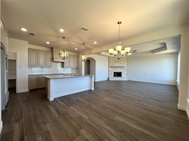 kitchen with a fireplace, decorative light fixtures, a chandelier, a kitchen island with sink, and light stone counters