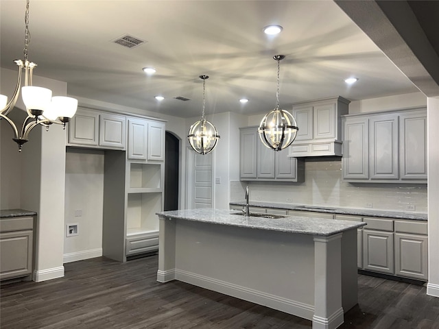 kitchen featuring arched walkways, a kitchen island with sink, a notable chandelier, a sink, and light stone countertops