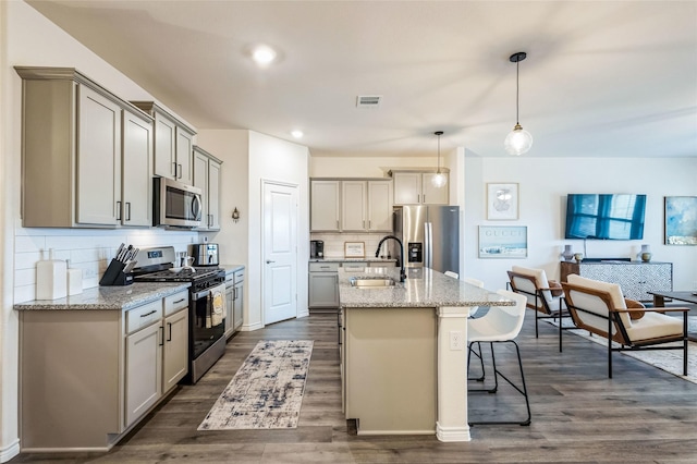 kitchen featuring visible vents, a breakfast bar, stainless steel appliances, gray cabinetry, and a sink