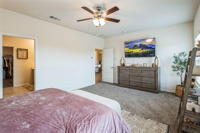 carpeted bedroom featuring a ceiling fan, baseboards, visible vents, wet bar, and a walk in closet