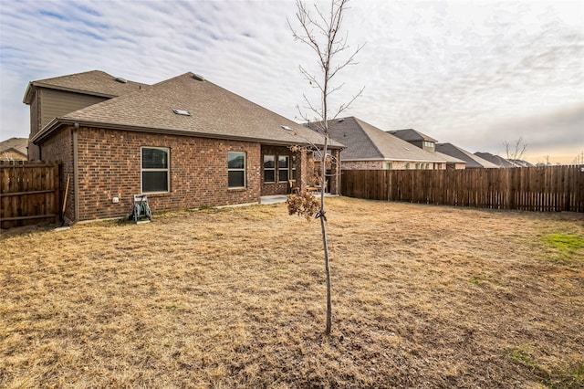 rear view of house with a fenced backyard, a shingled roof, and brick siding