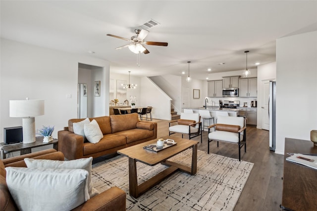 living area with dark wood finished floors, recessed lighting, visible vents, stairway, and ceiling fan with notable chandelier