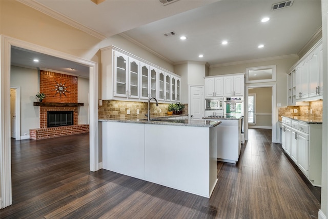 kitchen with light stone counters, ornamental molding, kitchen peninsula, a fireplace, and white cabinets