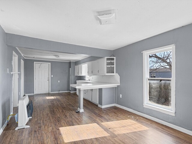 kitchen with heating unit, white cabinetry, dark hardwood / wood-style flooring, a kitchen bar, and kitchen peninsula