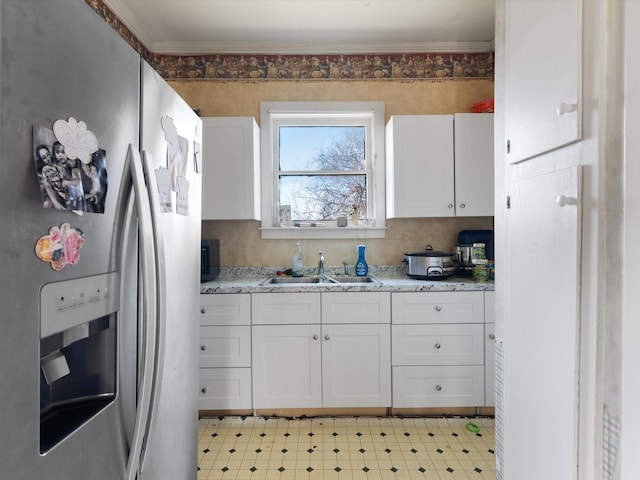 kitchen featuring sink, white cabinetry, crown molding, stainless steel fridge, and light stone countertops